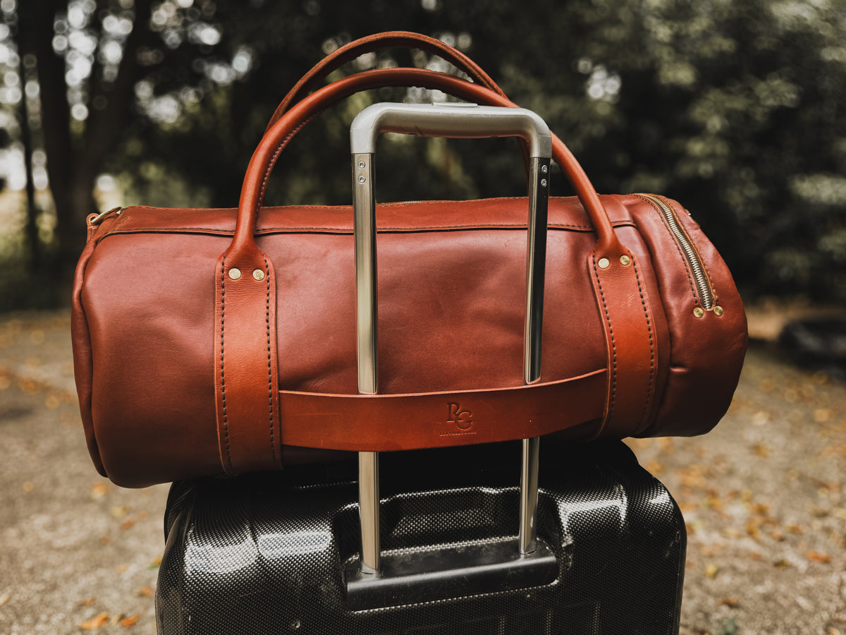 The Bully full-grain leather duffel bag secured to a rolling suitcase using its built-in trolley strap.
