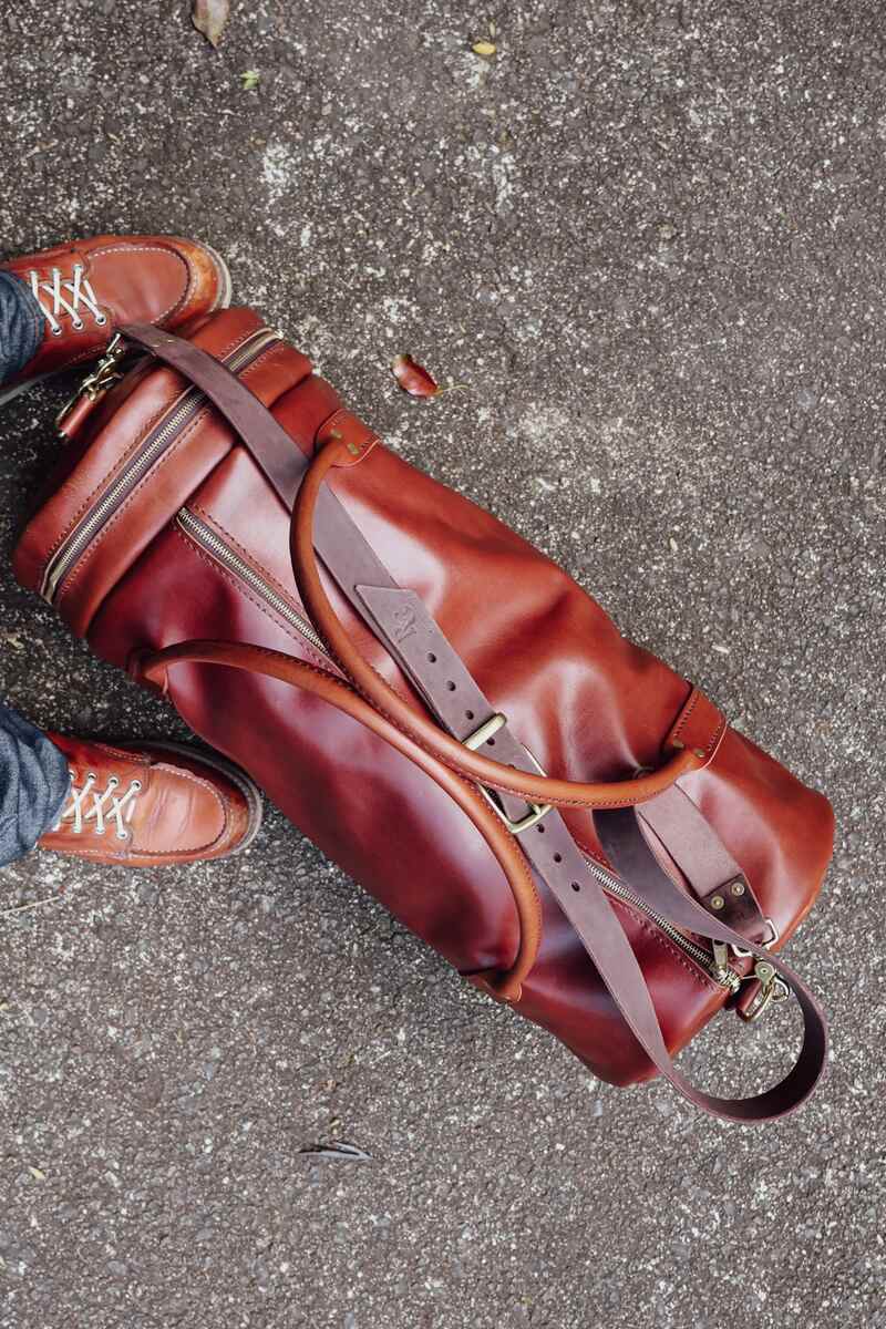 overhead view of The Bully full-grain Duffel Bag in chestnut brown on pavement beside a pair of heritage Moc-toe boots