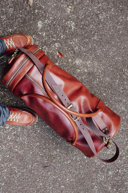 overhead view of The Bully full-grain Duffel Bag in chestnut brown on pavement beside a pair of heritage Moc-toe boots